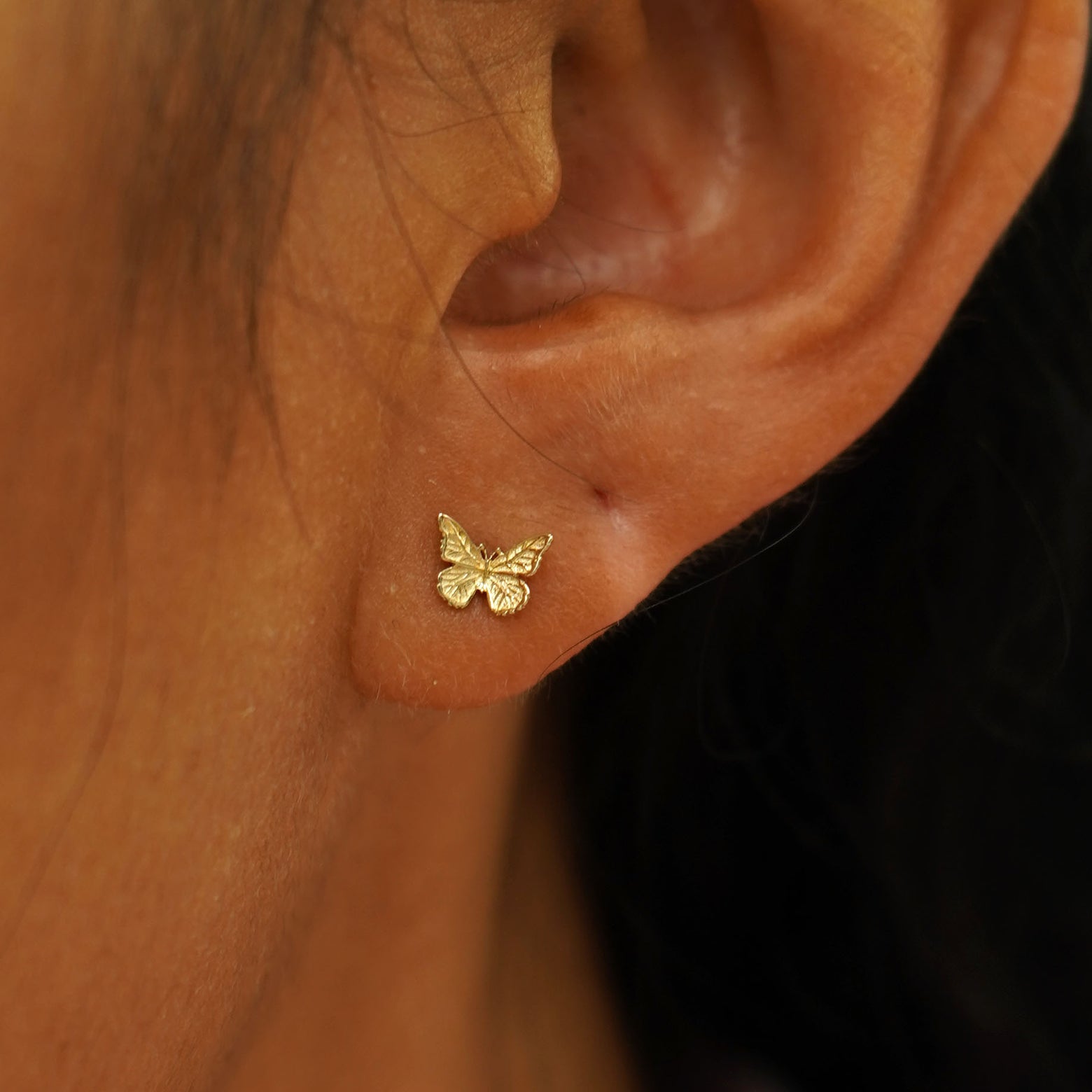 A model's ear wearing a 14k  gold Mini Butterfly Earring