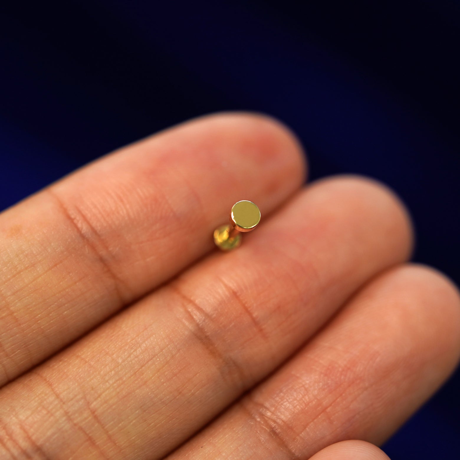 A solid yellow gold Mini Circle Flatback Piercing laying facedown on a model's finger to show the end of the flat back