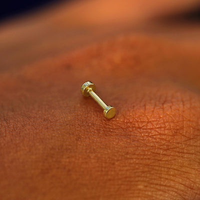 A solid 14k yellow gold Mini Circle Flatback Piercing resting on the back of a model's hand