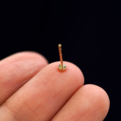 A yellow gold Mini Circle Earring laying facedown on a model's fingers to show the underside view