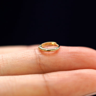 A yellow gold Mini Curvy Huggie Hoop Earring laying sideways on a model's fingertips