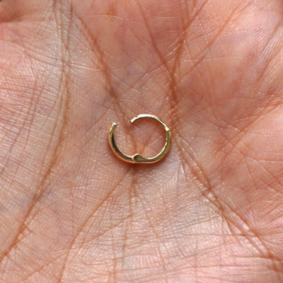 A solid 14k yellow gold Mini Curvy Huggie Hoop Earring open in a model's palm to show the hinge