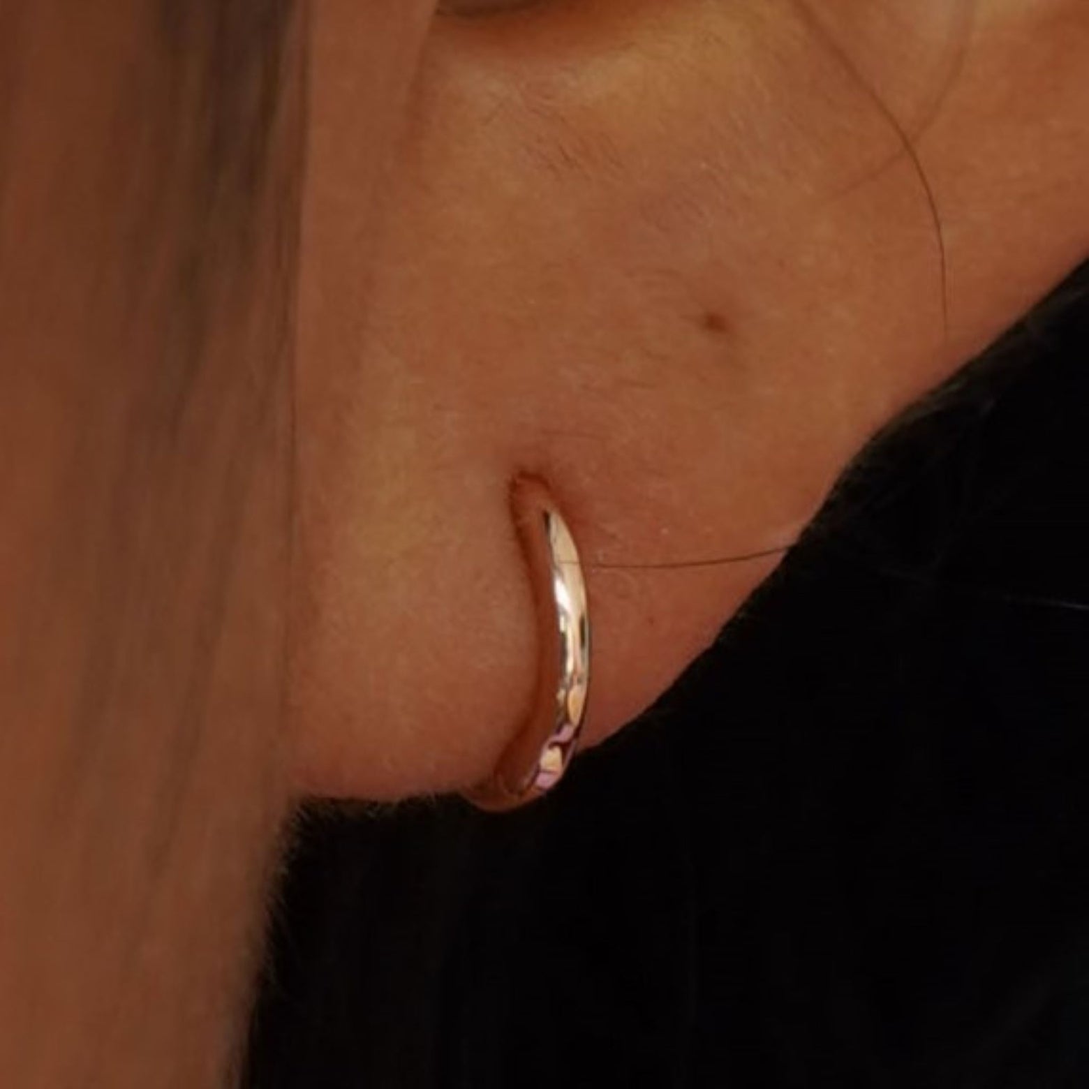 Close up view of a model's ear wearing a yellow gold Mini Curvy Huggie Hoop
