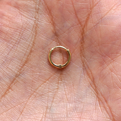 A solid 14k yellow gold Mini Curvy Huggie Hoop Earring closed in a model's palm