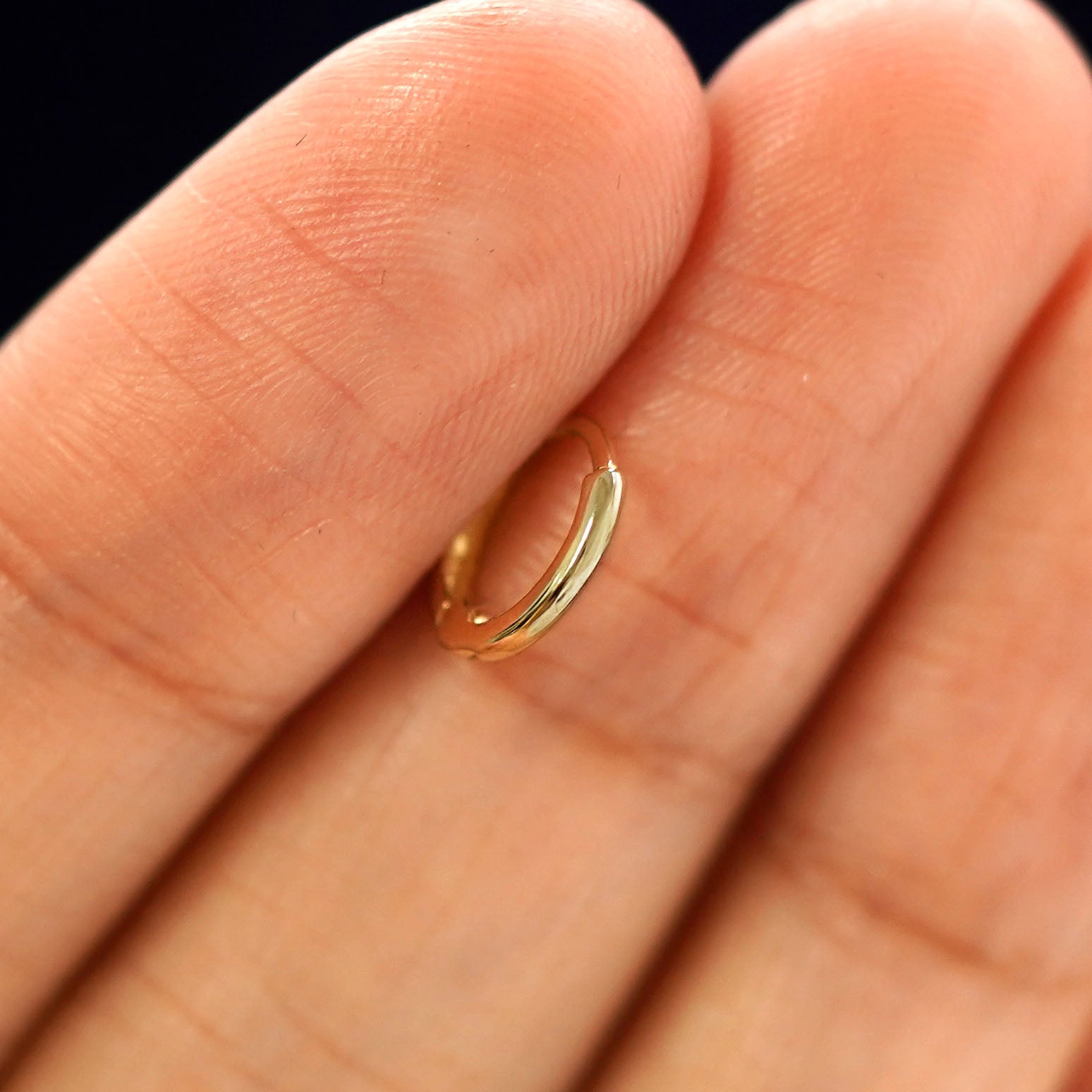 A 14k gold Mini Curvy Huggie Hoop Earring held in between a model's fingers to show the hoops thickness