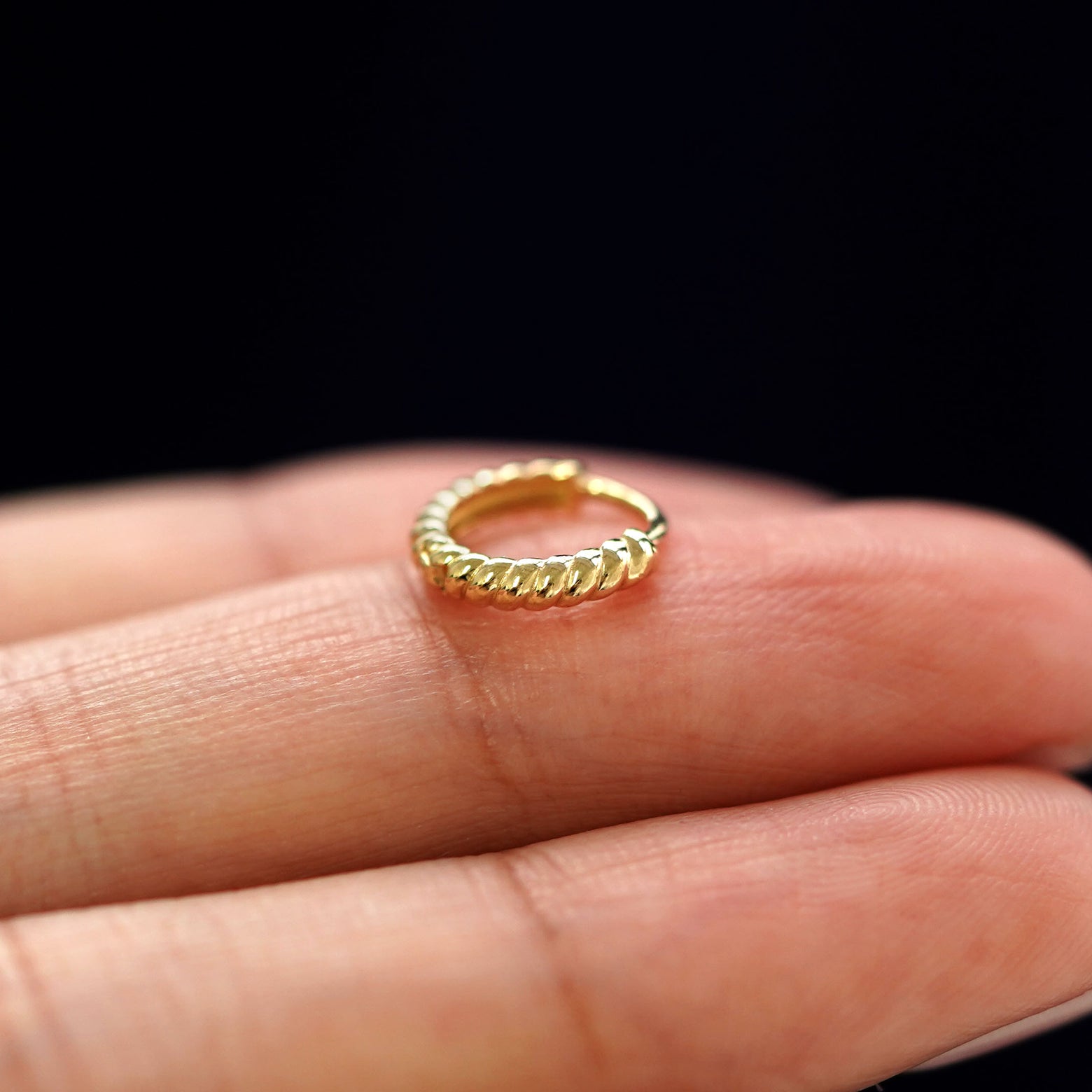 A yellow gold Mini Rope Huggie Hoop Earring laying sideways on a model's fingertips