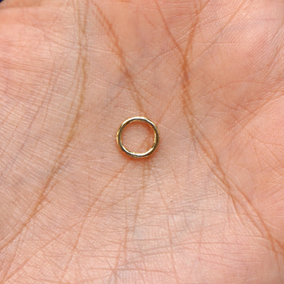 A model holding a closed yellow gold Mini Seamless Huggie Hoop in their palm