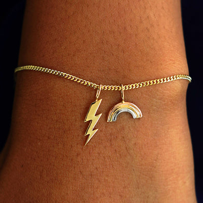 A model's wrist wearing a yellow gold Mini Miami Chain with a Lightning Bolt Charm and a Tattoo Machine Charm