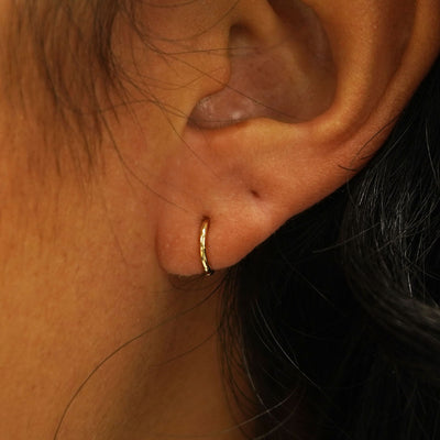 A model's ear wearing a 14k gold Mini Seamless Huggie Hoop / Piercing