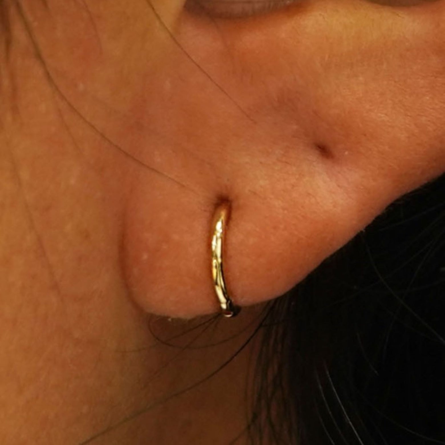 Close up view of a model's ear wearing a yellow gold Mini Seamless Huggie Hoop / Piercing