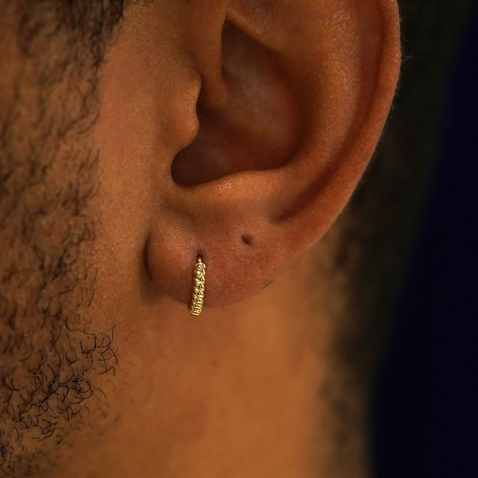 A model's ear wearing a 14k gold Mini Rope Huggie Hoop Earring