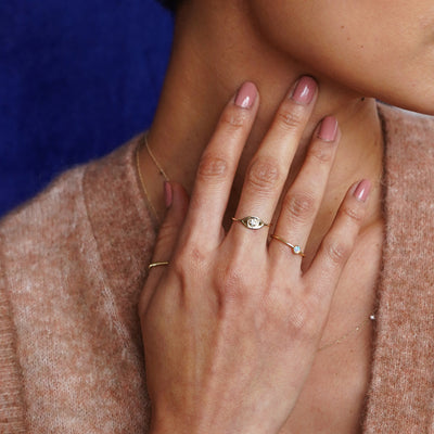 A model touching their neck wearing a Diamond Evil Eye Ring, a Rope Ring, and a Moonstone Ring