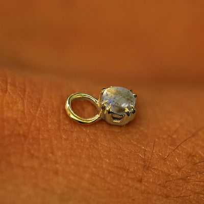 A solid yellow gold Labradorite Charm for earring resting on the back of a model's hand