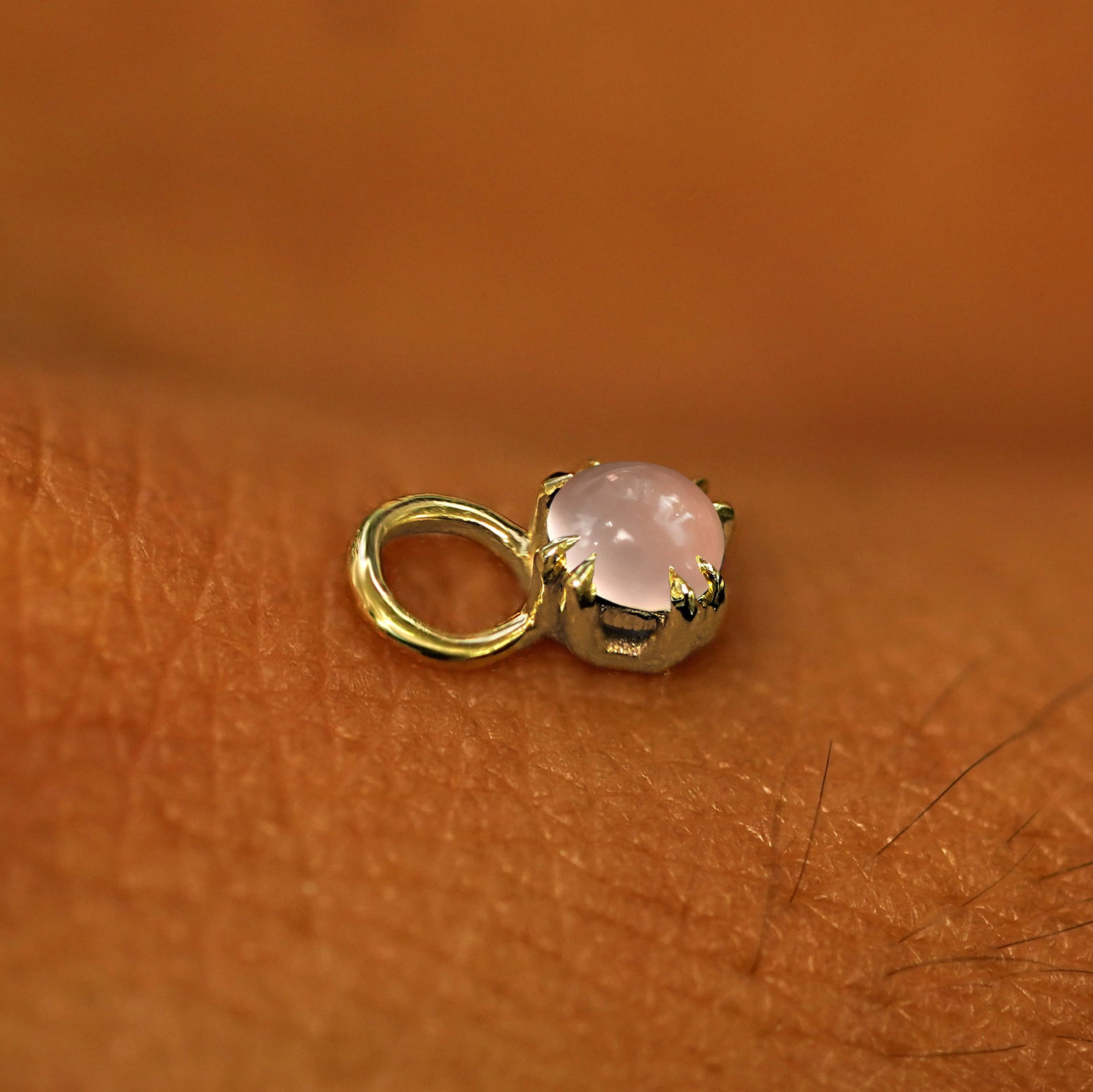 A solid yellow gold Rose Quartz Charm for earring resting on the back of a model's hand