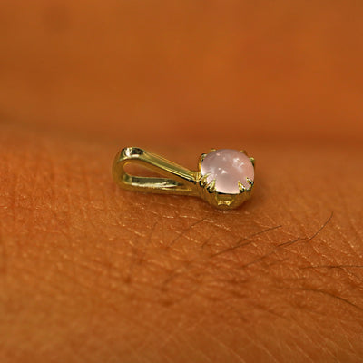 A 14k yellow gold Rose Quartz Charm for chain resting on the back of a model's hand