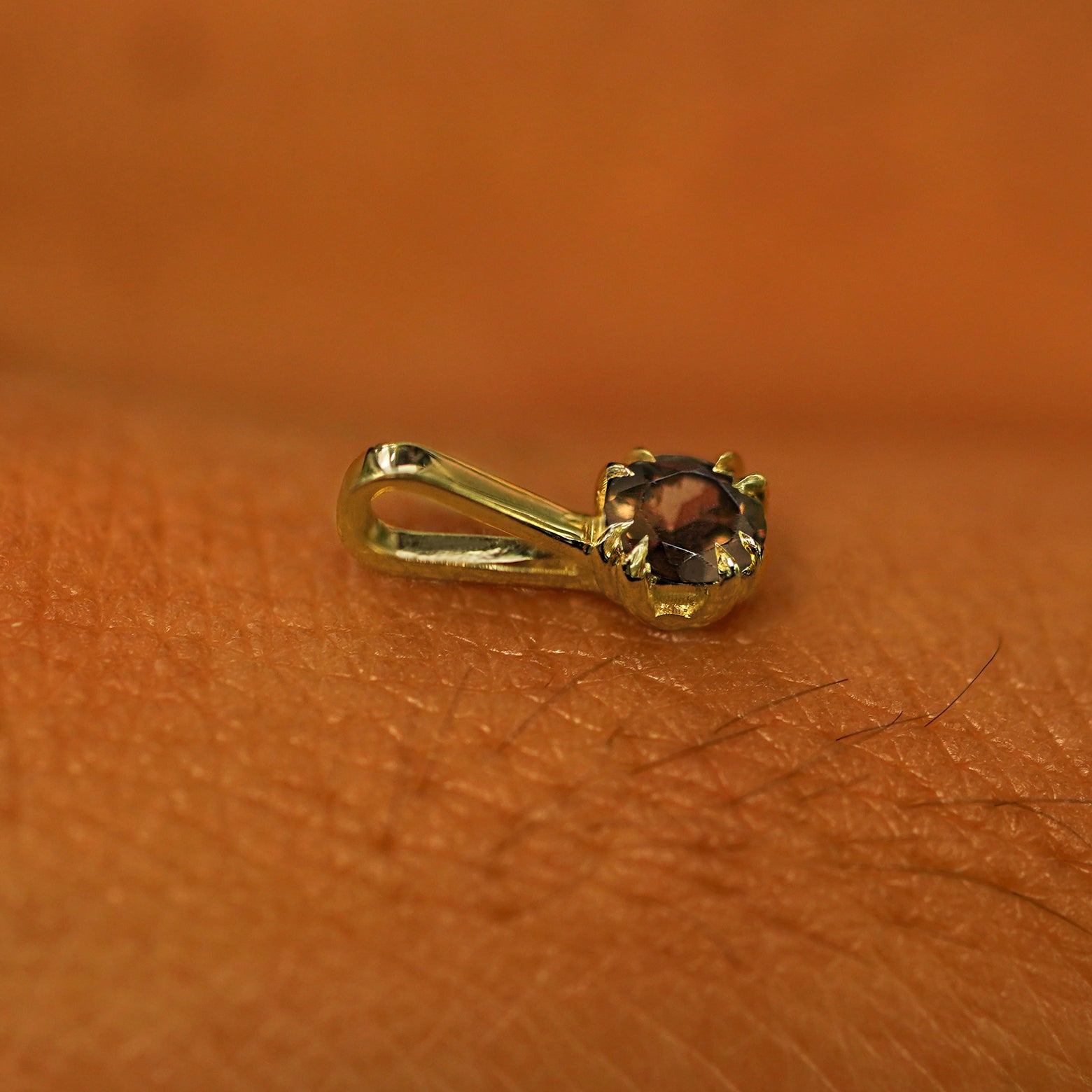 A 14k yellow gold Smoky Quartz Charm for chain resting on the back of a model's hand