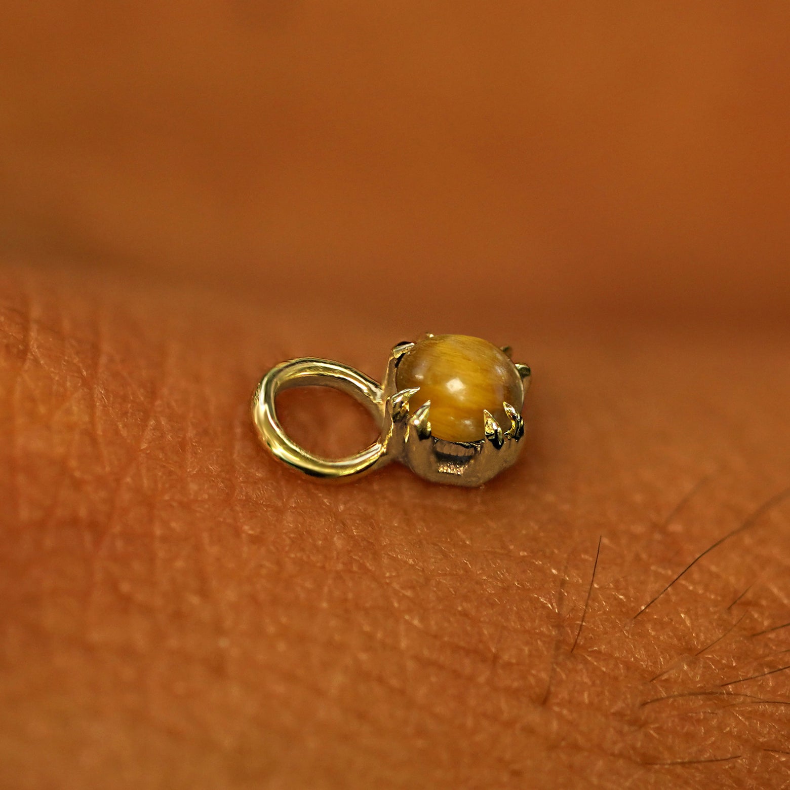 A solid yellow gold Tiger Eye Charm for earring resting on the back of a model's hand