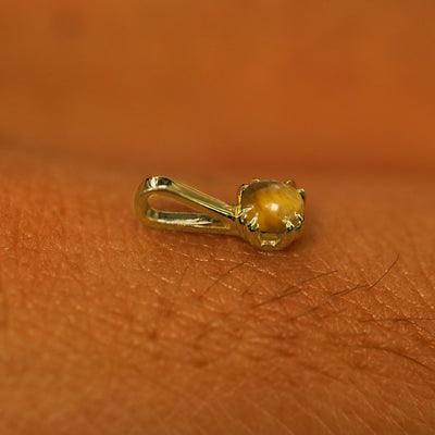 A 14k yellow gold Tiger Eye Charm for chain resting on the back of a model's hand