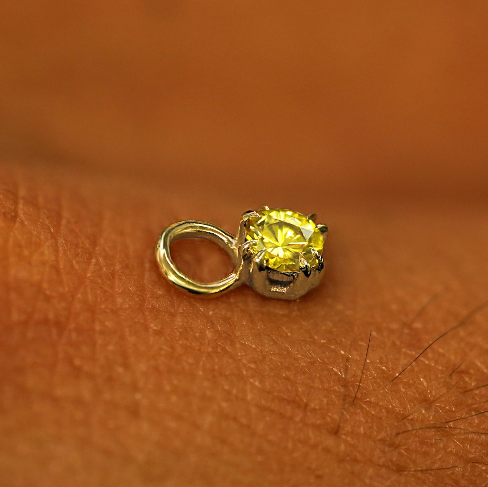 A solid yellow gold Yellow Diamond Charm for earring resting on the back of a model's hand