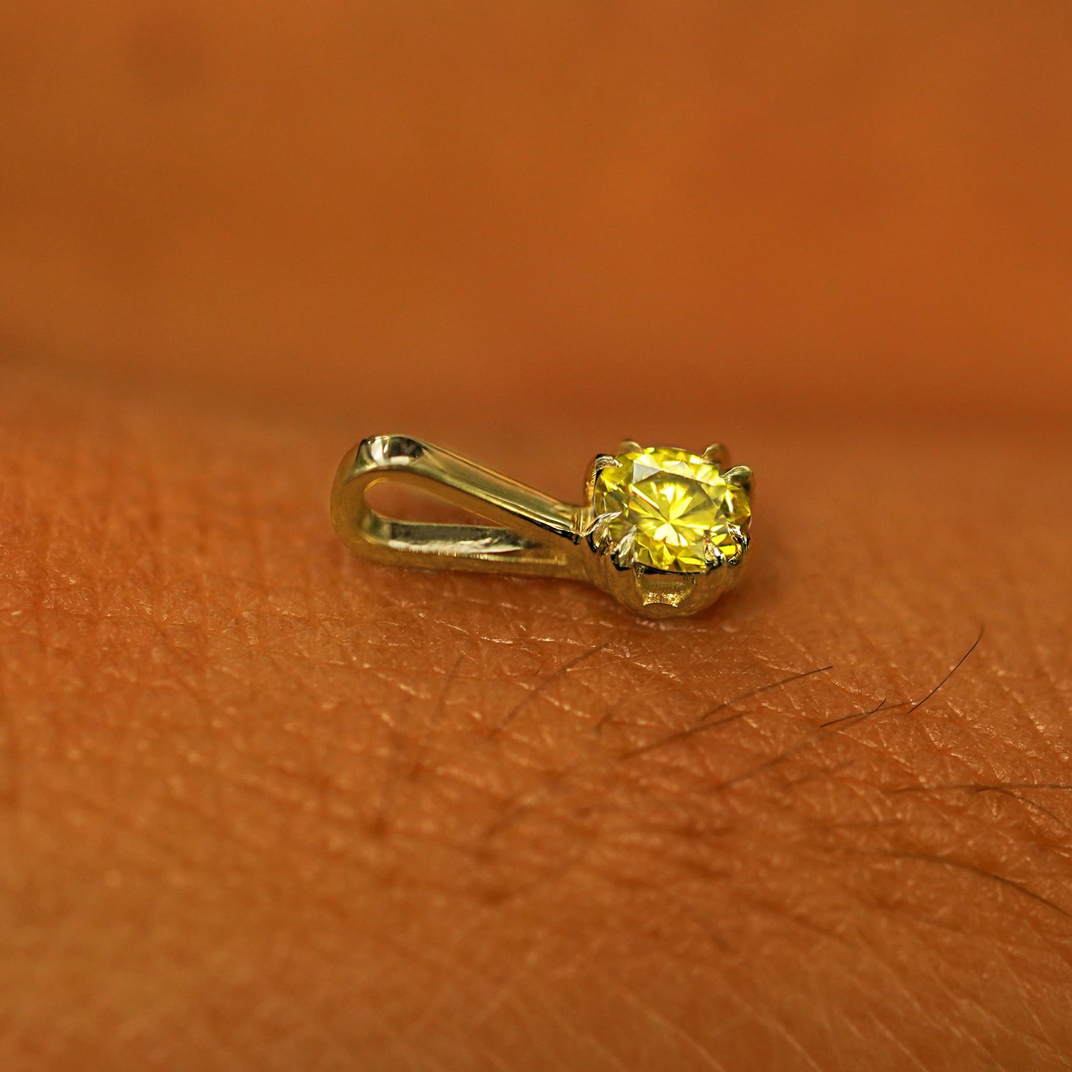 A 14k yellow gold Yellow Diamond Charm for chain resting on the back of a model's hand
