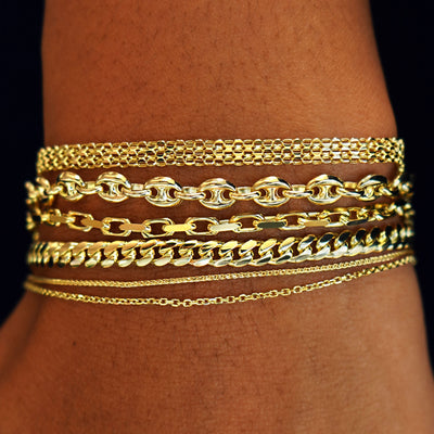 A  model's wrist wearing  yellow gold Bismarck, Puffy Mariner, Anchor, Medium Miami, Wheat, and Medium Cable chains