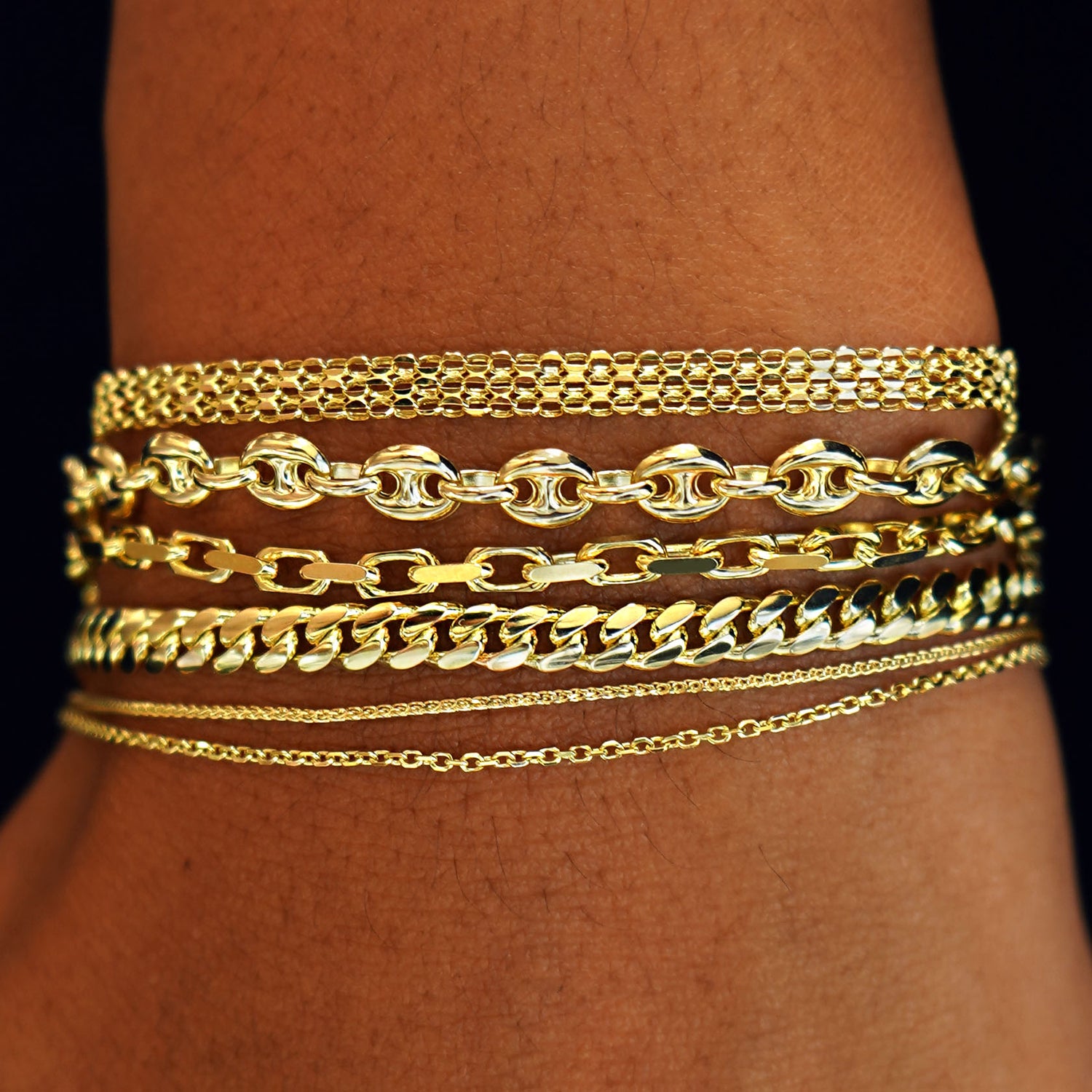 A model's wrist wearing yellow gold Bismarck, Puffy Mariner, Anchor, Medium Miami, Wheat, and Medium Cable Bracelets