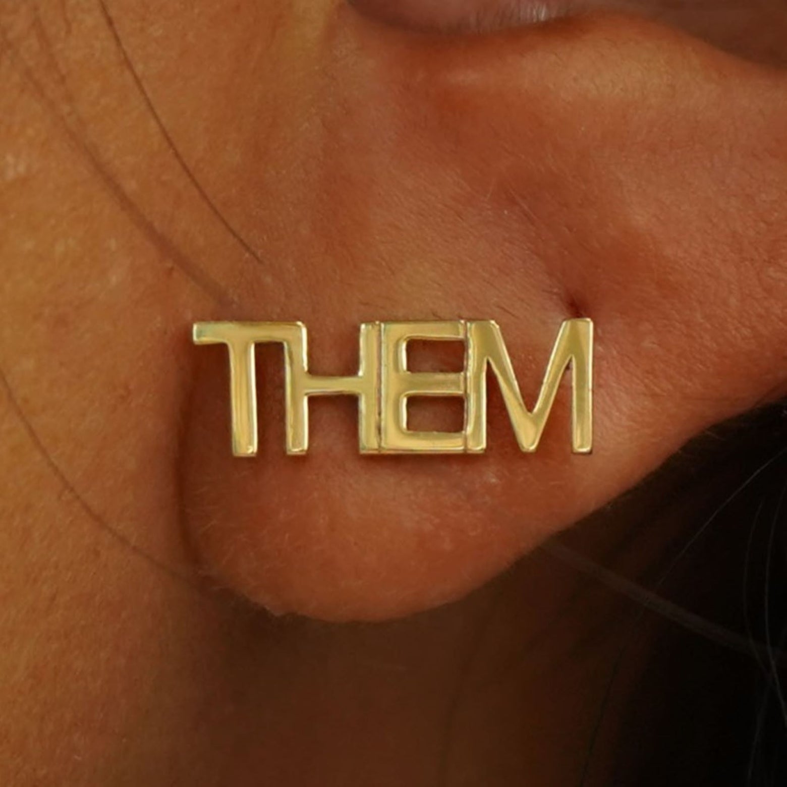 Close up view of a model's ear wearing a solid yellow gold Them Earring