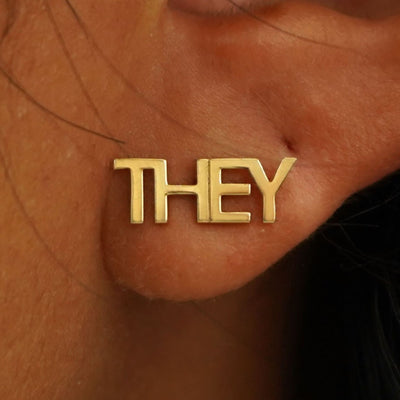 Close up view of a model's ear wearing a solid yellow gold They Earring