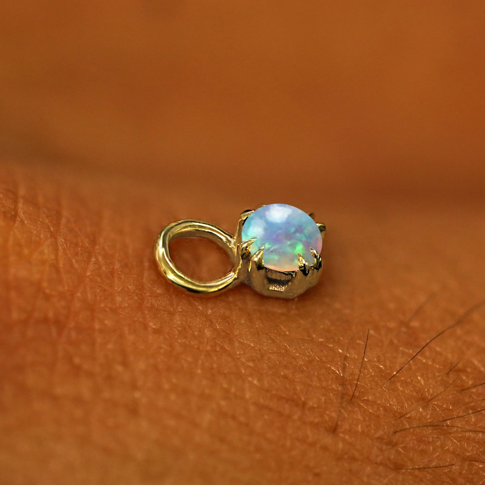 A solid yellow gold Opal Charm for earring resting on the back of a model's hand