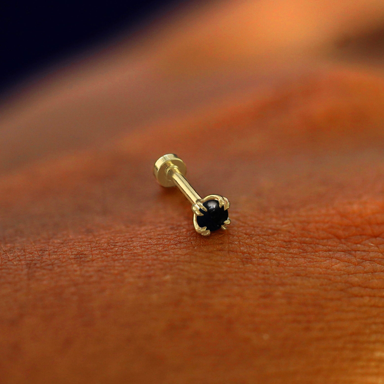 A solid 14k yellow gold Onyx Flatback Piercing resting on the back of a model's hand