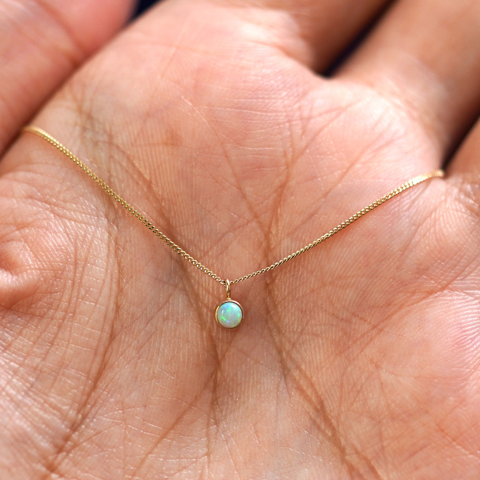 A solid 14k gold Opal Necklace resting in a models palm