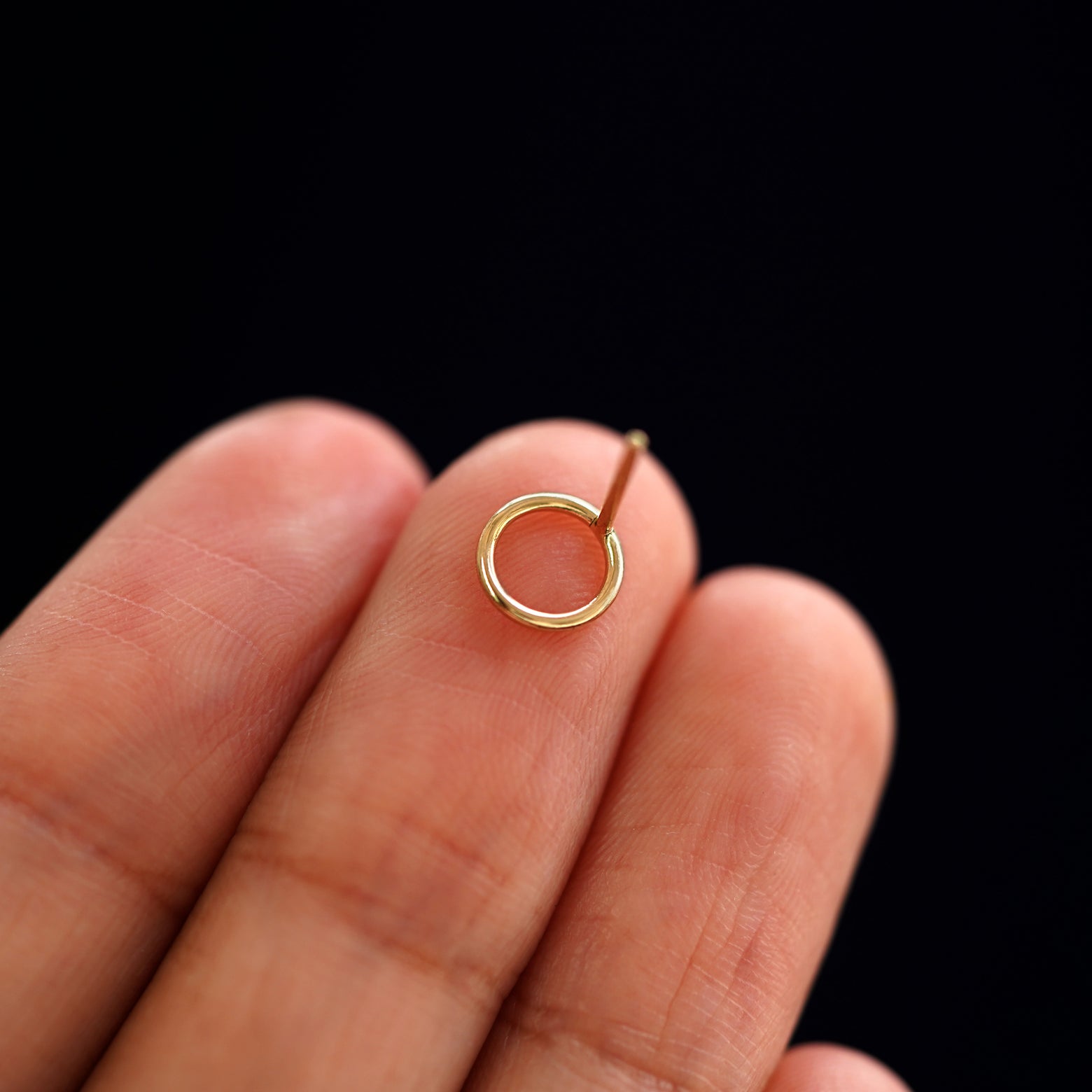 A yellow gold Open Circle Earring laying facedown on a model's fingers to show the underside view