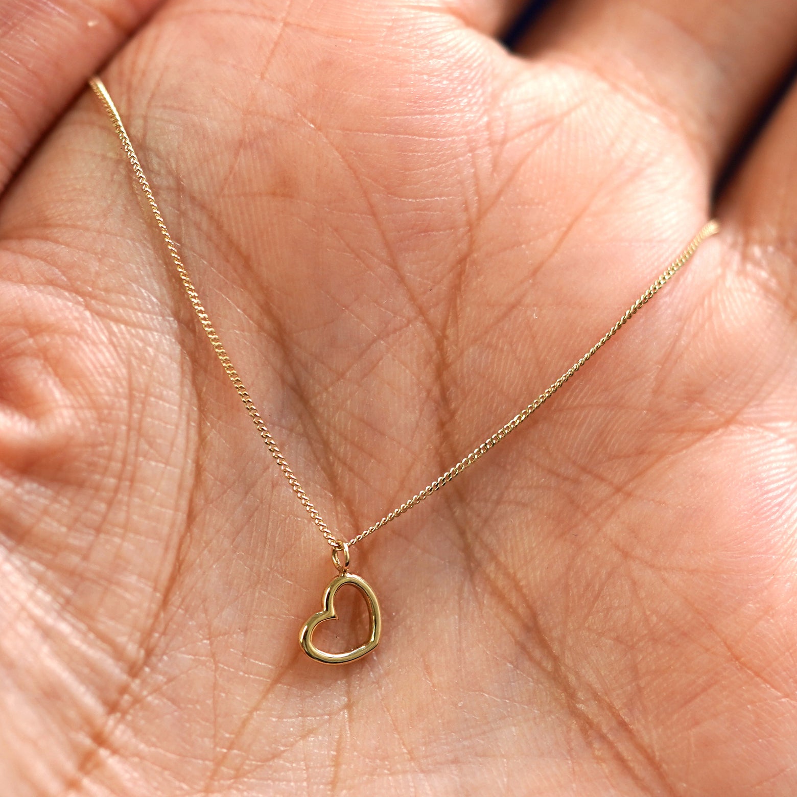 A yellow gold Heart Necklace draped on a model's palm