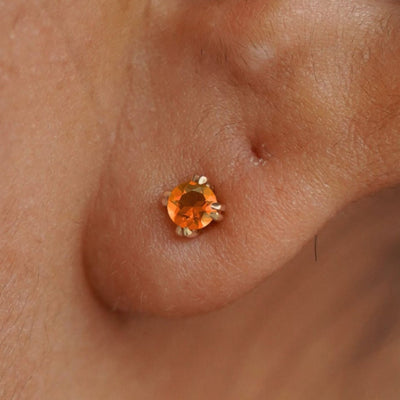 Close up view of a model's ear wearing a 14k yellow gold orange Fire Opal Earring