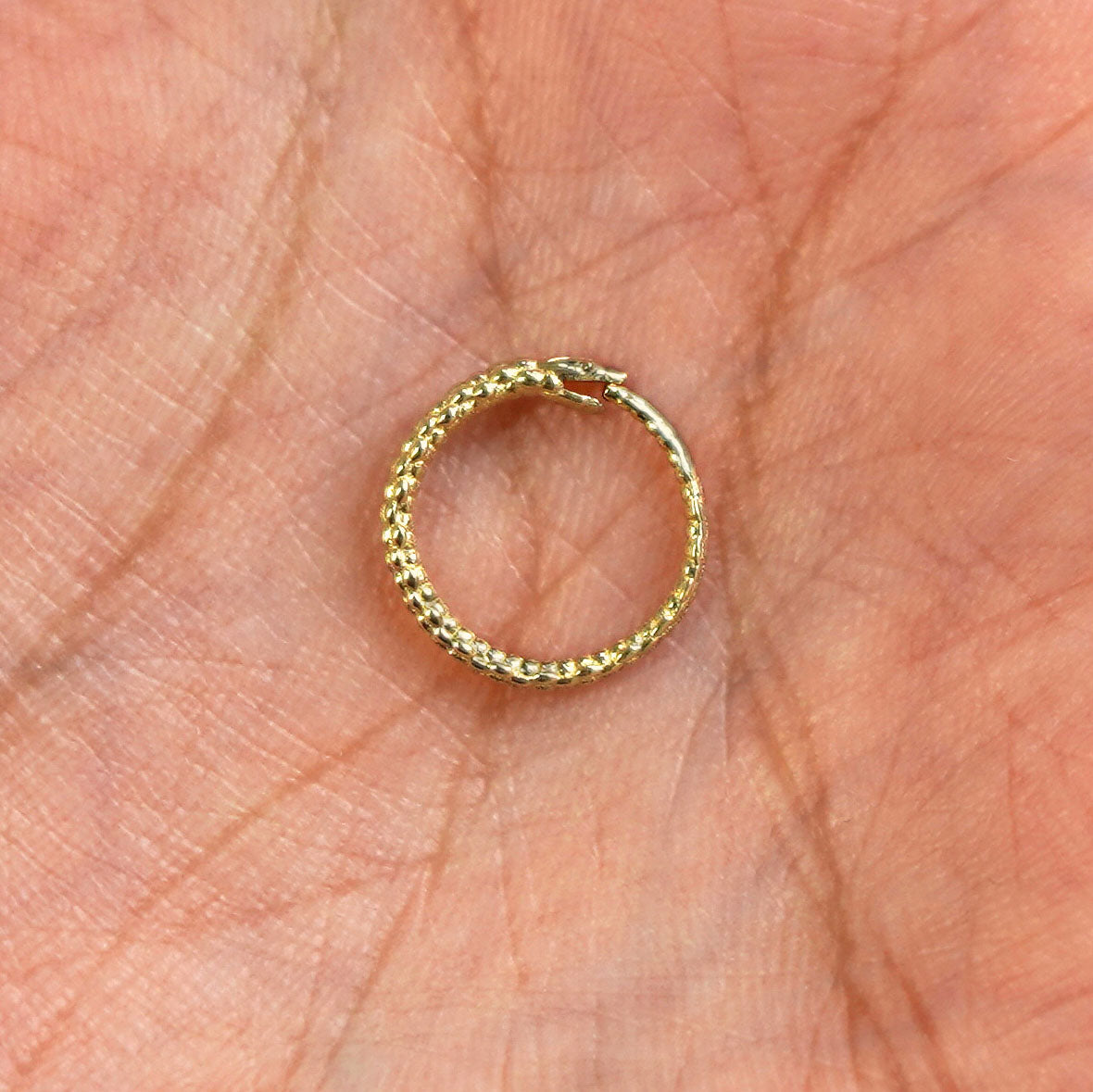 A 14 karat solid gold Snake Hoop / Piercing resting in a model's palm