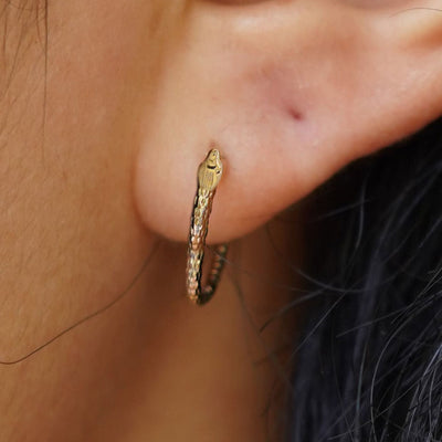 Close up view of a model's ear wearing a yellow gold Snake Hoop / Piercing