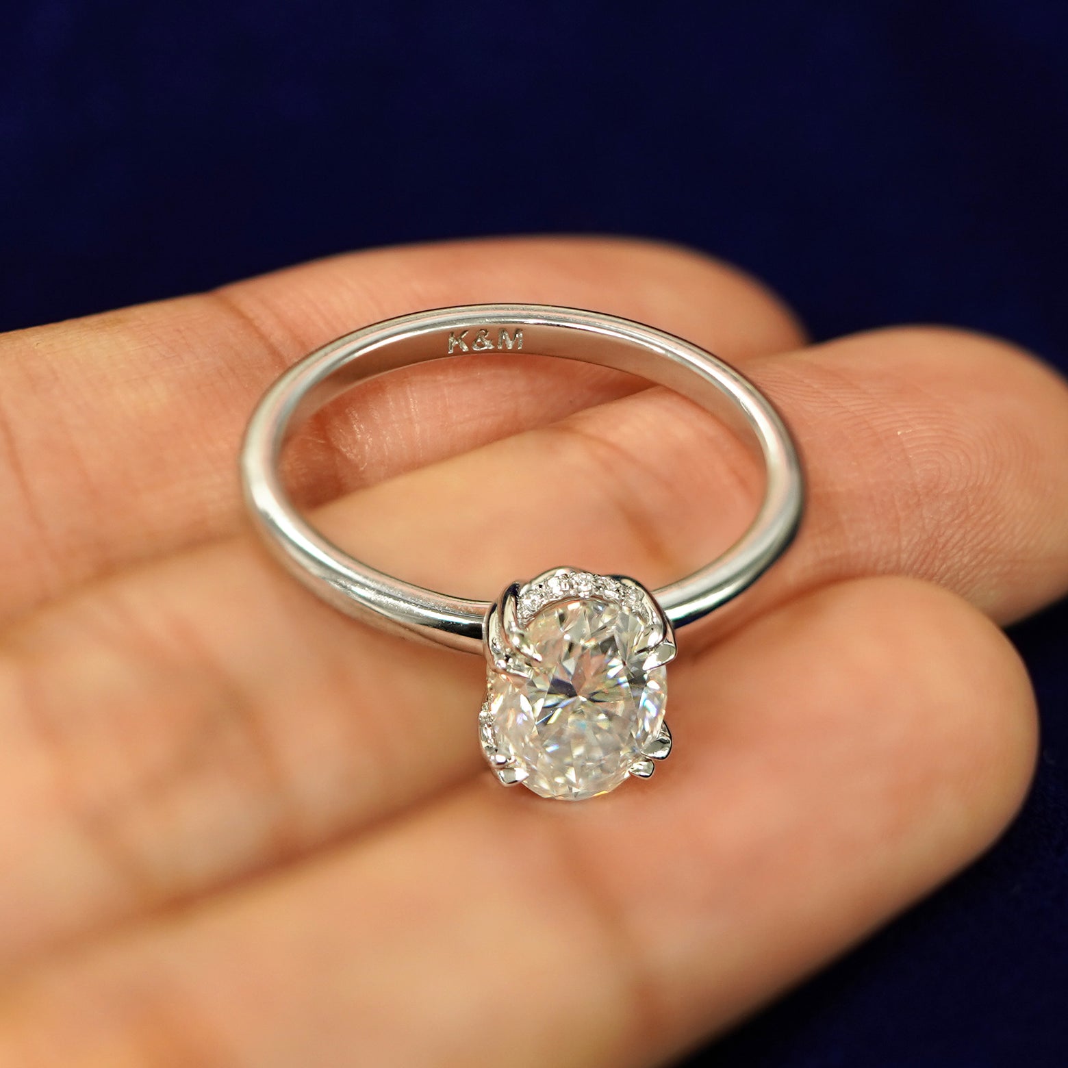 A 14k white gold Oval Moissanite Halo Ring tilted slightly to show K & M engraved inside the band