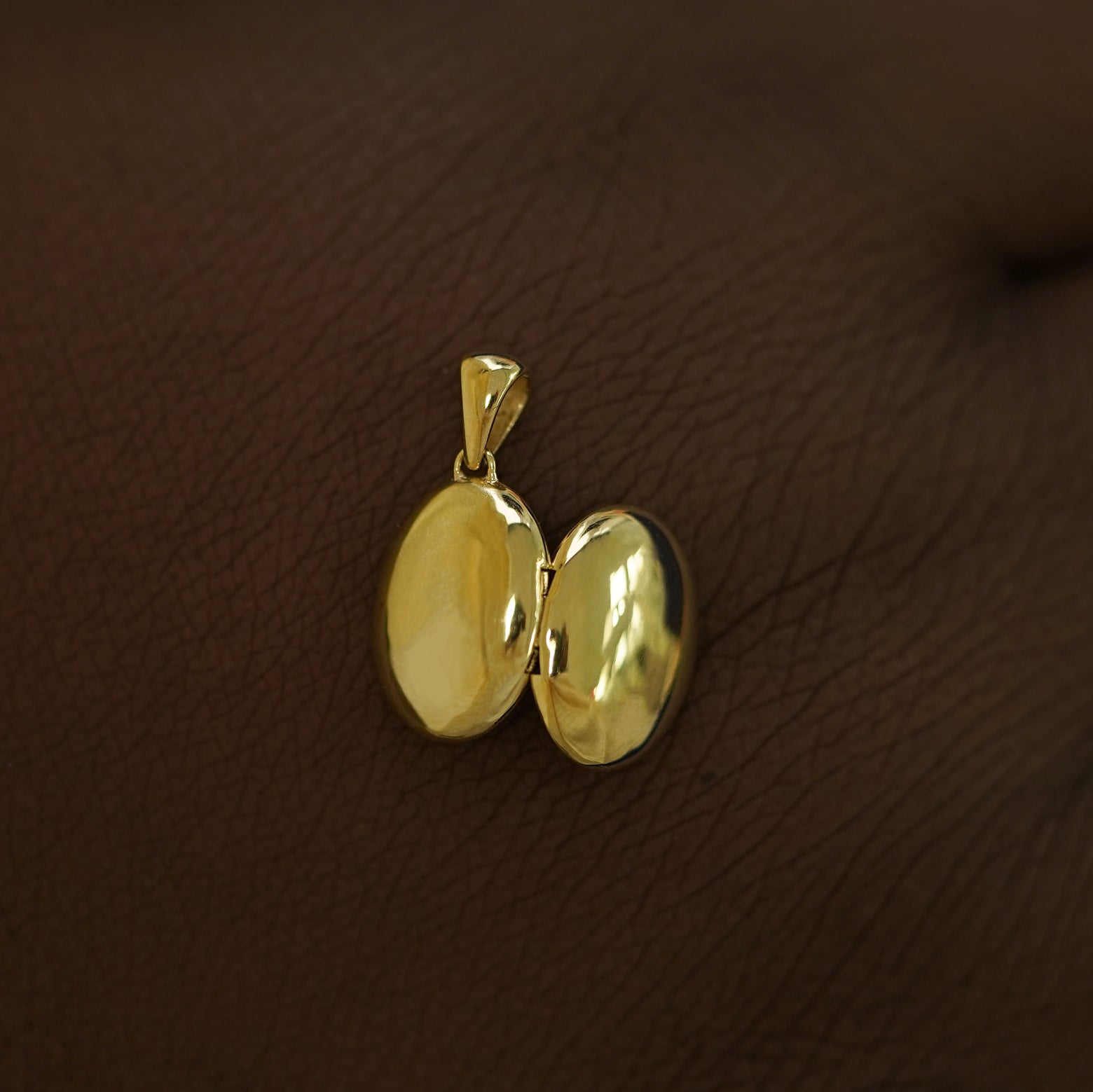 An open 14k yellow gold Oval Locket Pendant on the back of a model's hand showing the outside of the pendant