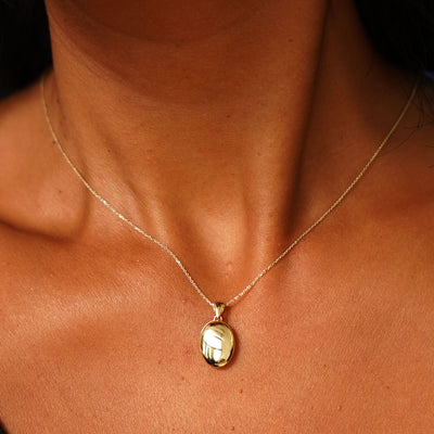 Close up view of a model's neck wearing a yellow gold Oval Locket Pendant on a Cable Chain