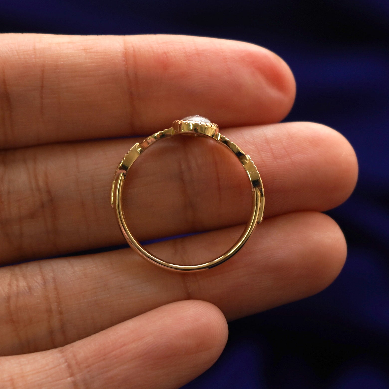 A yellow gold Pear Salt and Pepper Diamond Leaves Ring in a model's hand showing the thickness of the band