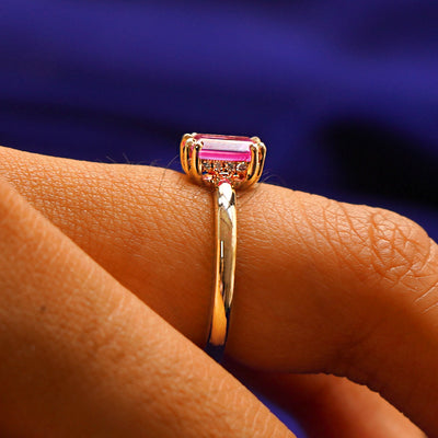 Side view of a Emerald Cut Pink Sapphire Ring on a model's finger to show the hidden halo