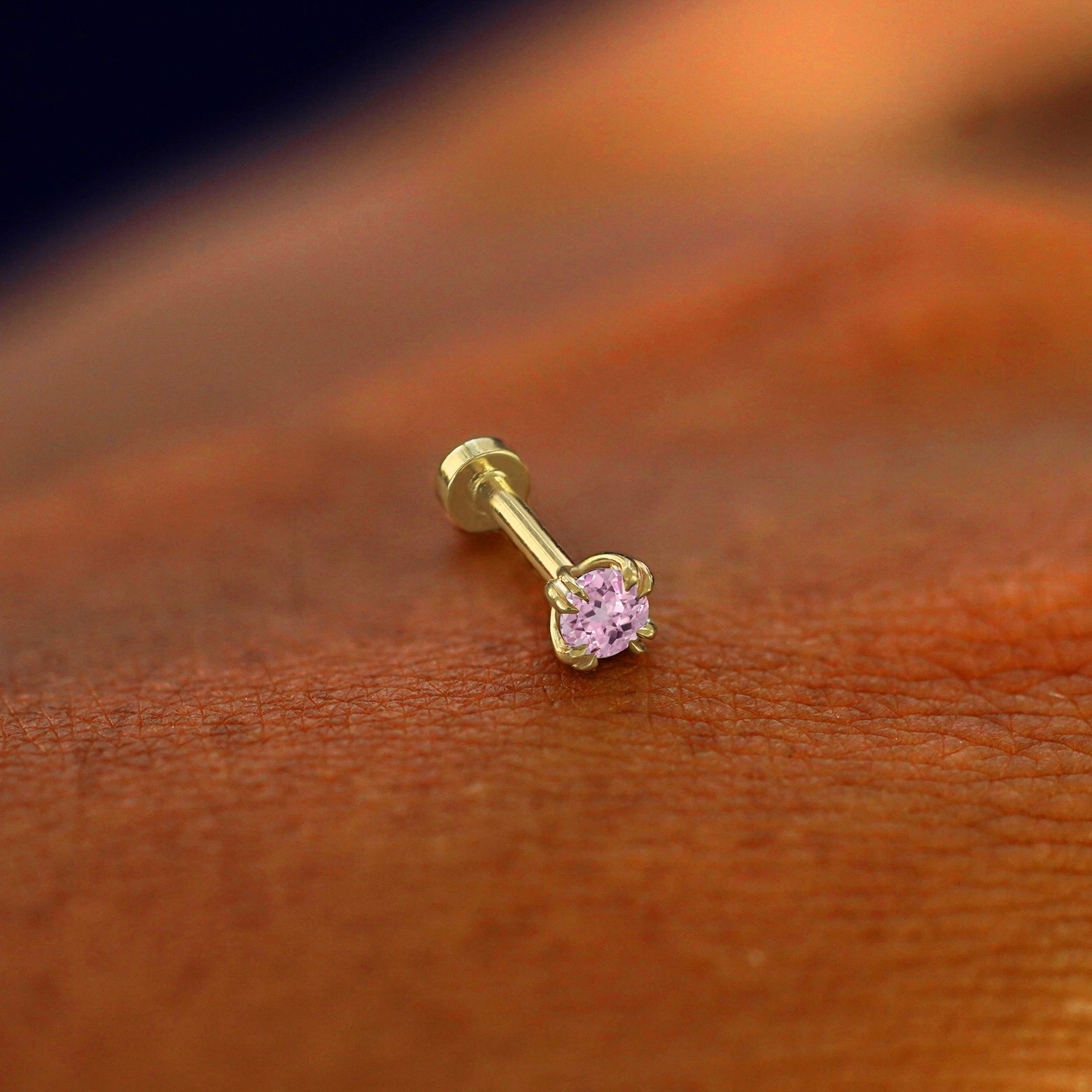 A solid 14k yellow gold Pink Sapphire Flatback Piercing resting on the back of a model's hand