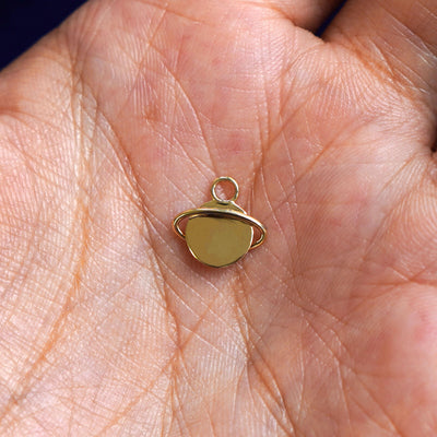 A 14k gold Saturn Charm for chain resting in a model's palm to show the underside of the charm