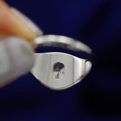 A Platinum Oval Diamond Signet Ring held by a model's fingertips to show the underside of the ring