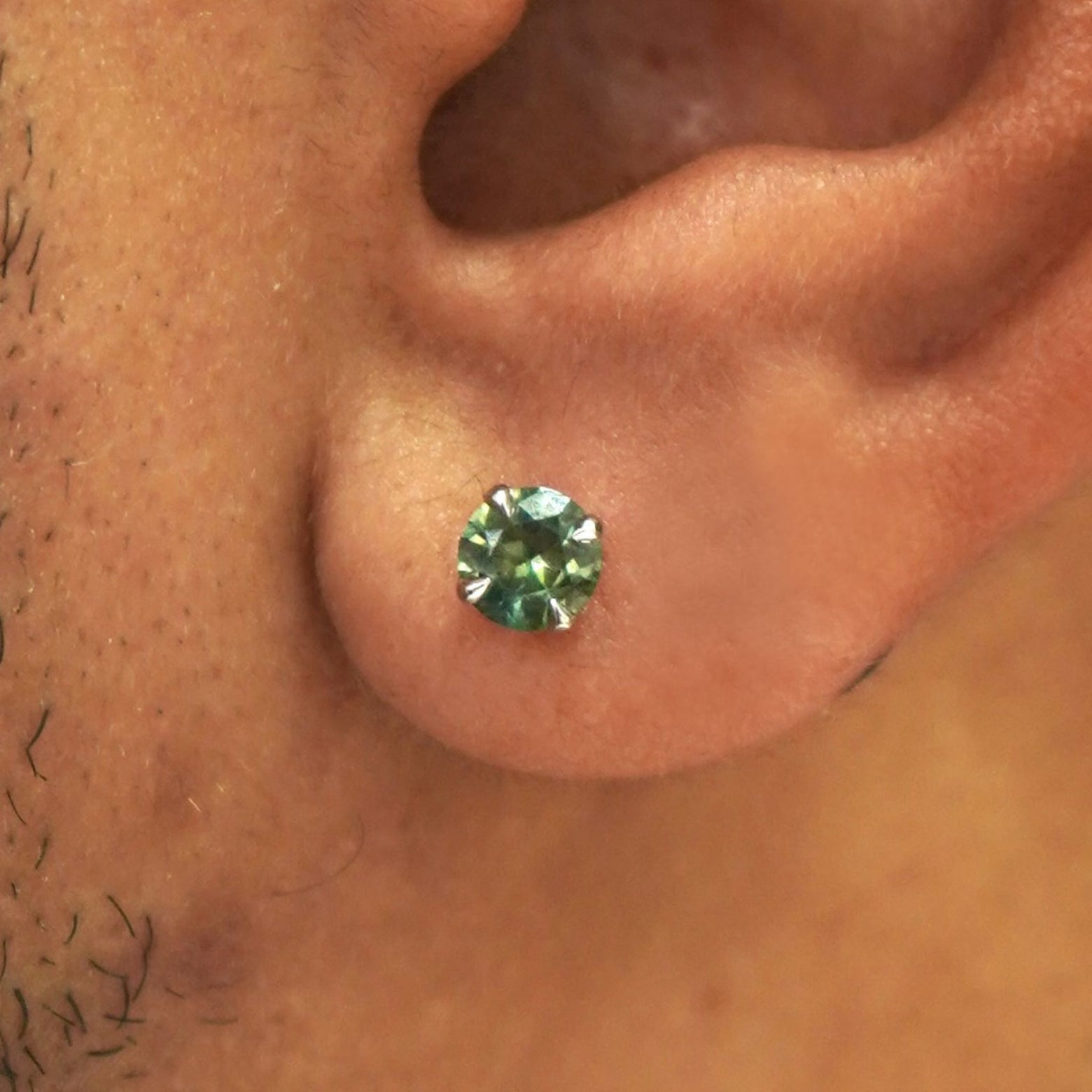 Close up view of a model's ear wearing a solid 14k gold green sapphire pressure lock earring