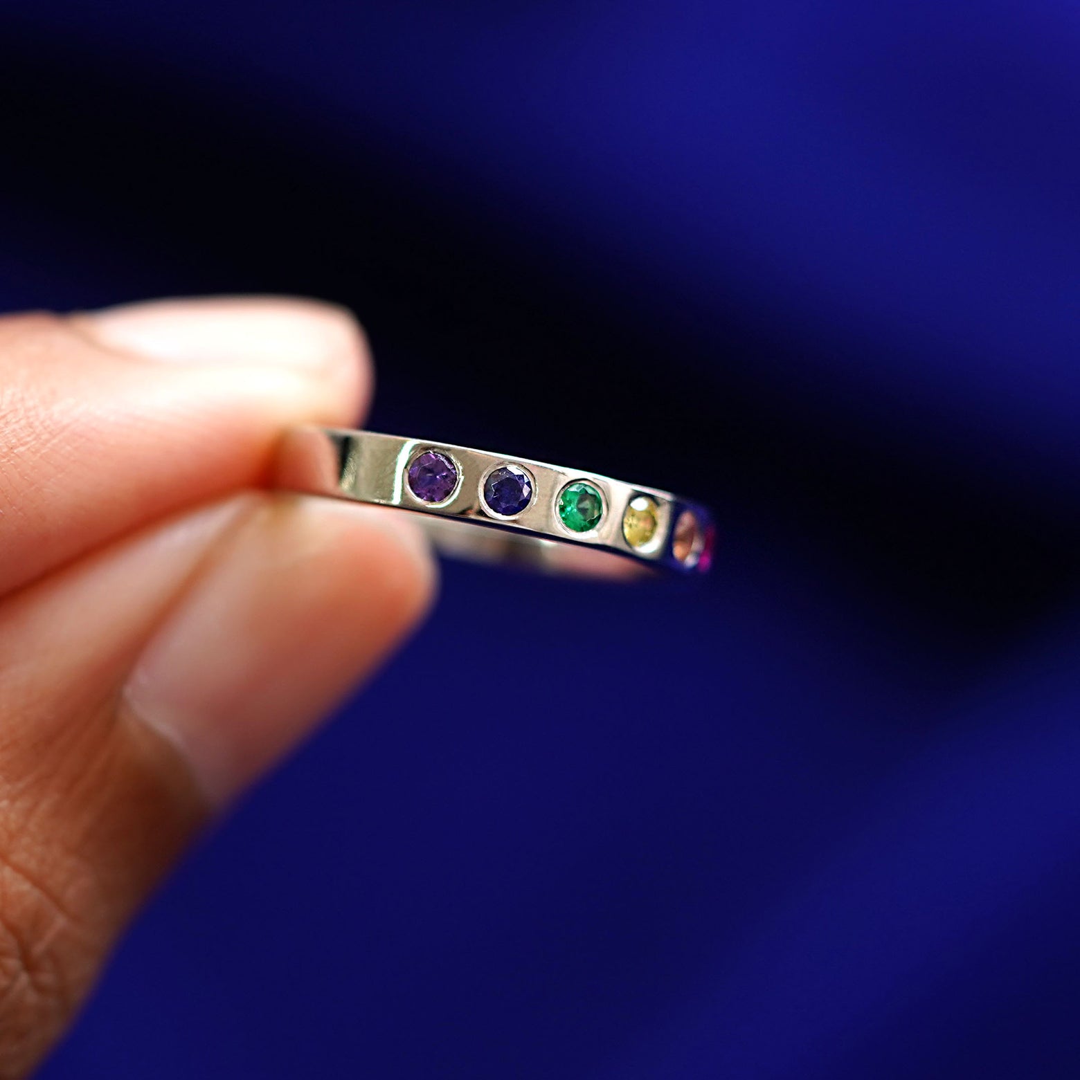 A solid yellow gold Rainbow Band turned to the side to show the yellow sapphire, emerald, blue sapphire, and purple sapphire