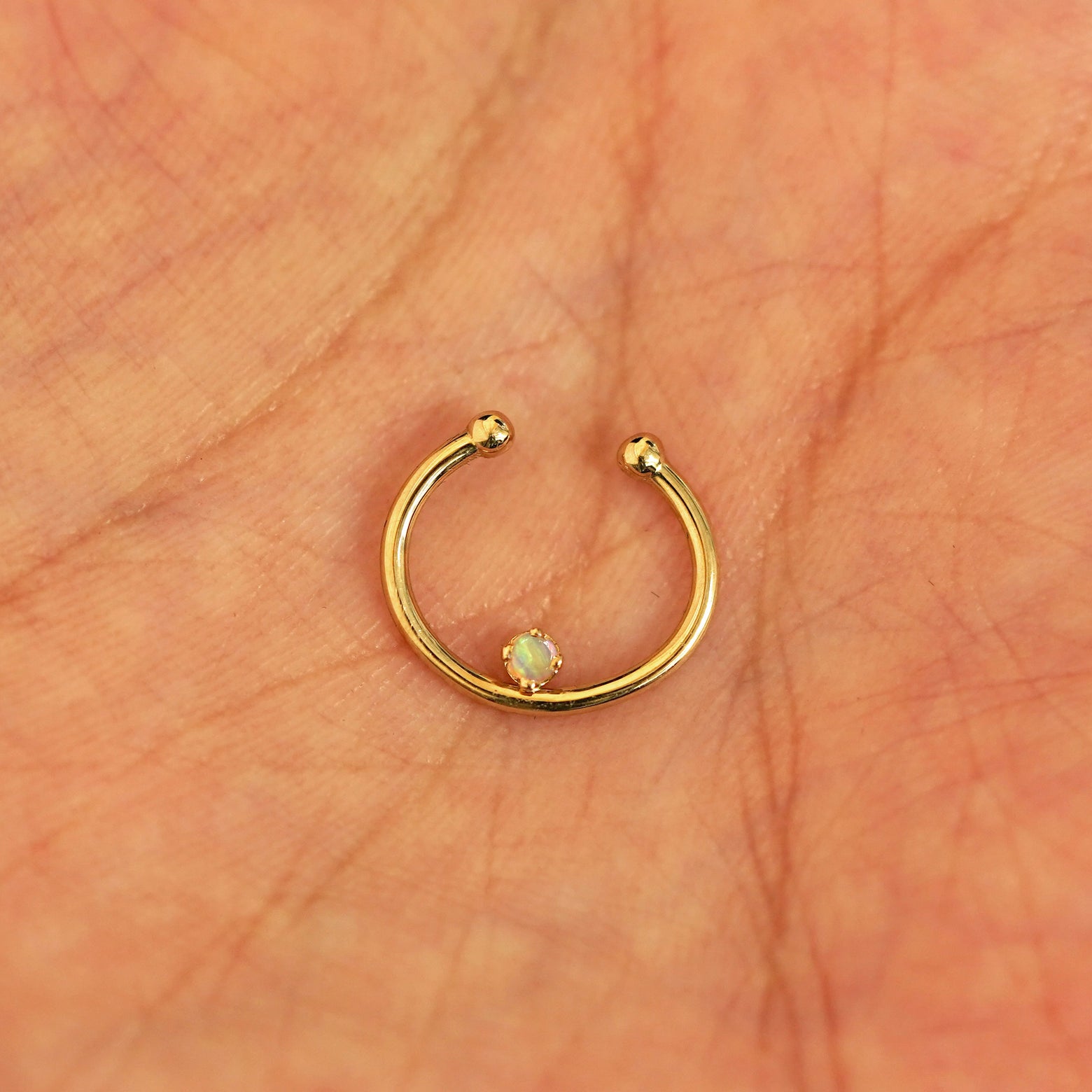 A model's hand holding a 14 karat yellow gold opal Non-Pierced Raised Gemstone Septum