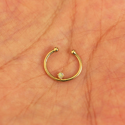 A model's hand holding a 14 karat yellow gold opal Non-Pierced Raised Gemstone Septum