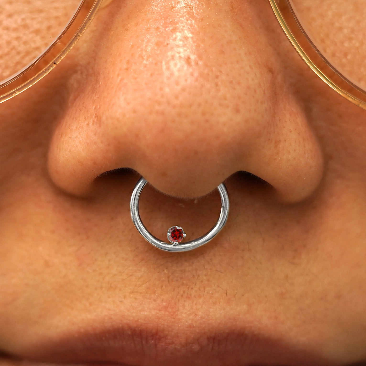 Close up view of a model's nose wearing a 14k white gold ruby Raised Gemstone Septum