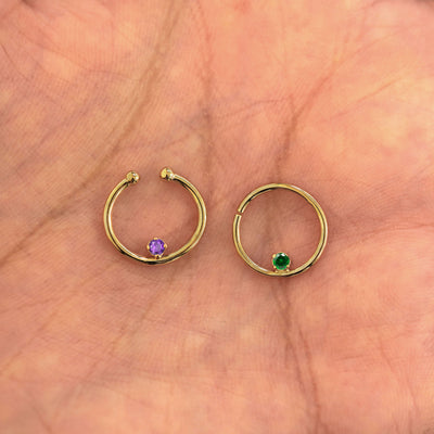 Two 14k gold Raised Gemstone Septum rings show in options of Non-Pierced and Pierced resting in the palm of a model's hand